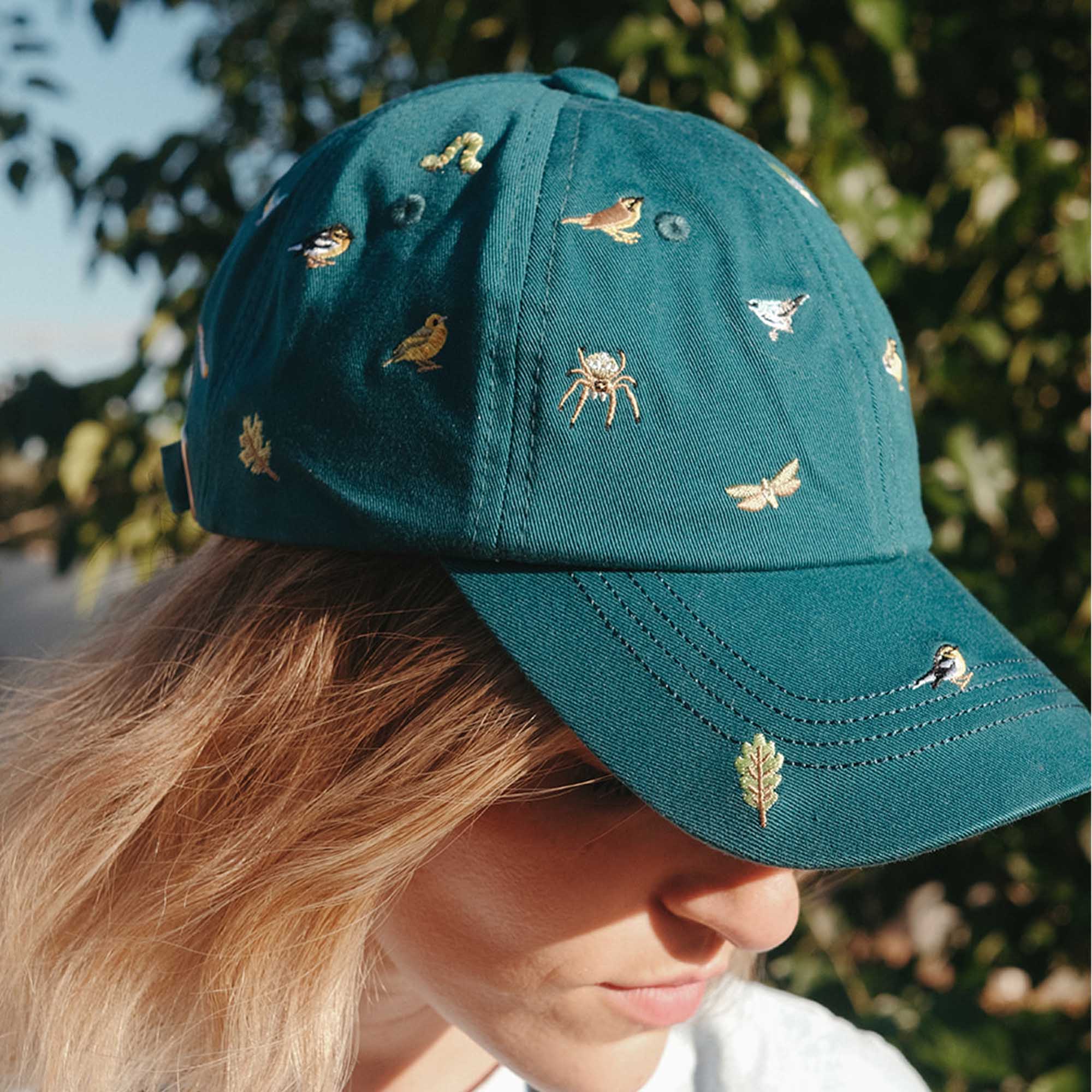 Teal cap with embroidered designs worn by a person outdoors