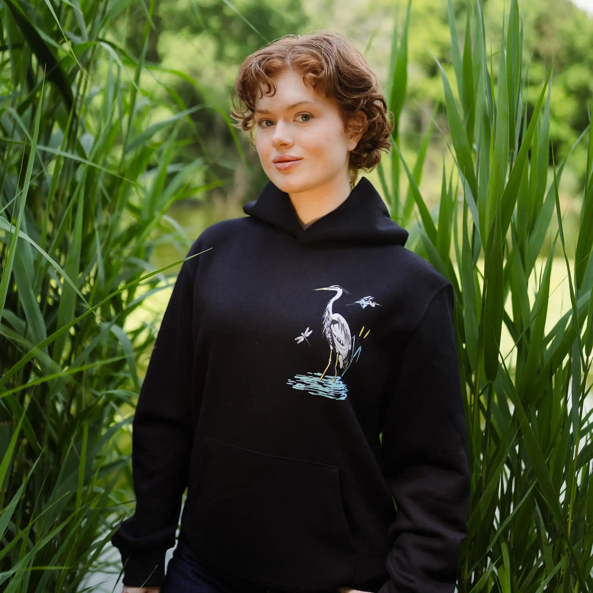 Person wearing a black hoodie with a heron design in a natural setting
