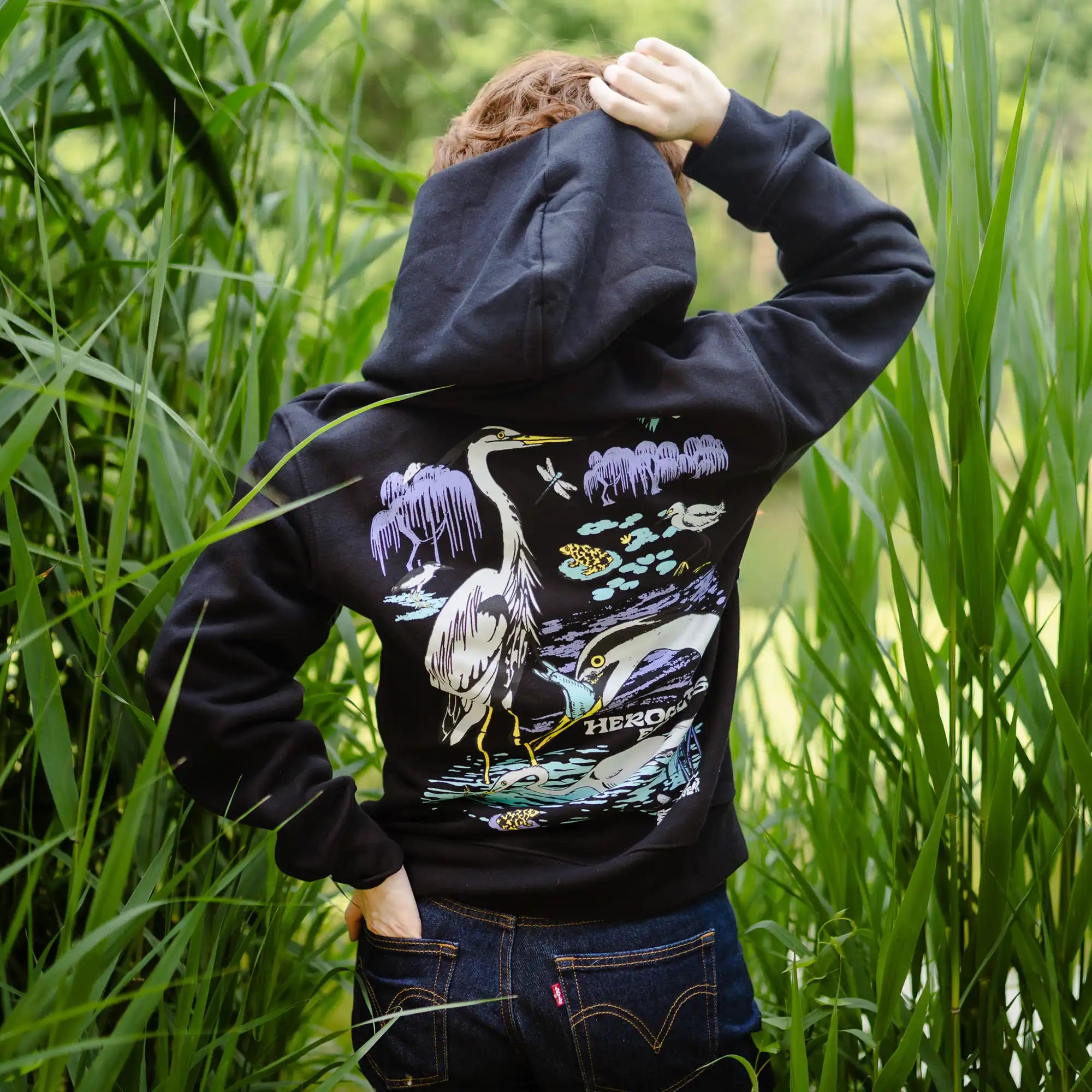 Person wearing a black hoodie with nature-themed design in a grassy area