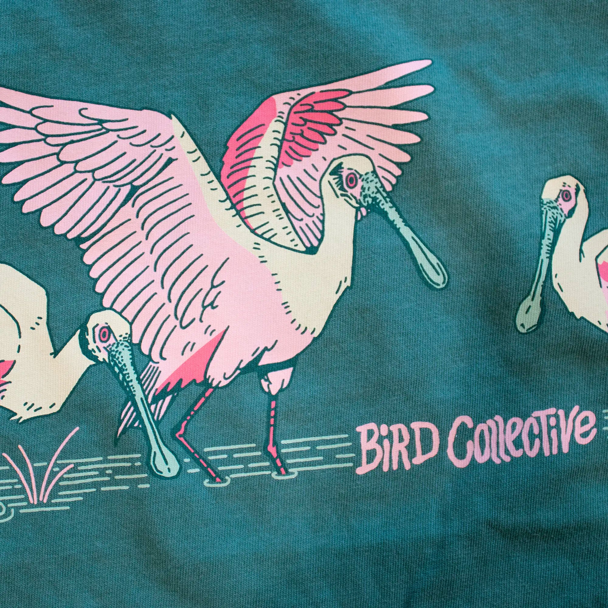 Photo detail of a gulf tide teal tee with three Roseate Spoonbills wading in shallow water and Bird Collective on the front.